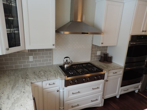River White with Gray Ceramic Subway Backsplash , White Ceramic Arabesque Tiles, White Kitchen Cabinets and Stainless Steel Vent Hood